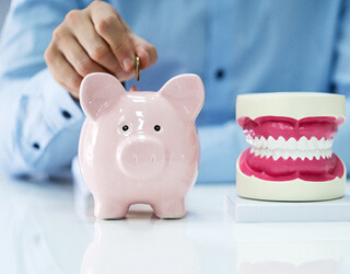 man placing coin in a piggy bank beside a model jaw