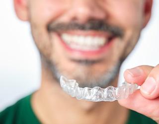 Closeup of patient in green shirt holding clear aligner