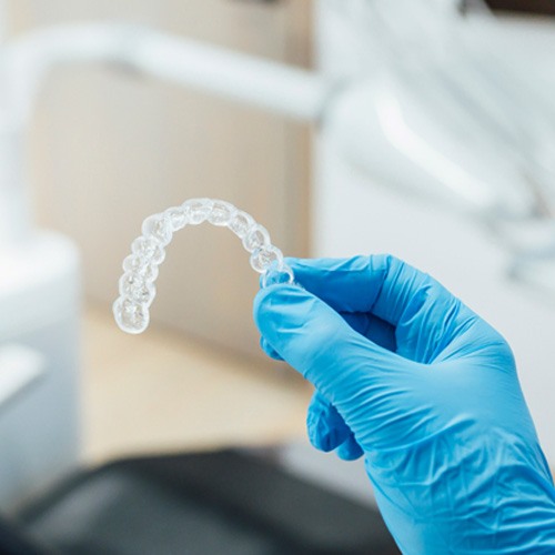 Dentist holding clear aligner with blue gloves